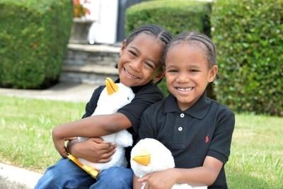 两位非裔美籍儿童(一男一女)坐着笑着并握着Aflac鸭子
